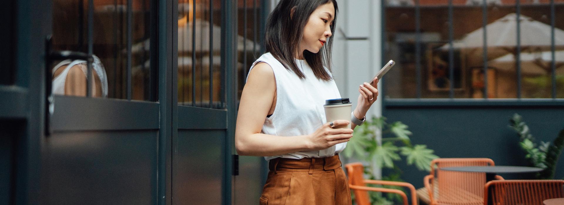 Woman with cell phone in one hand and coffee cup in the other hand