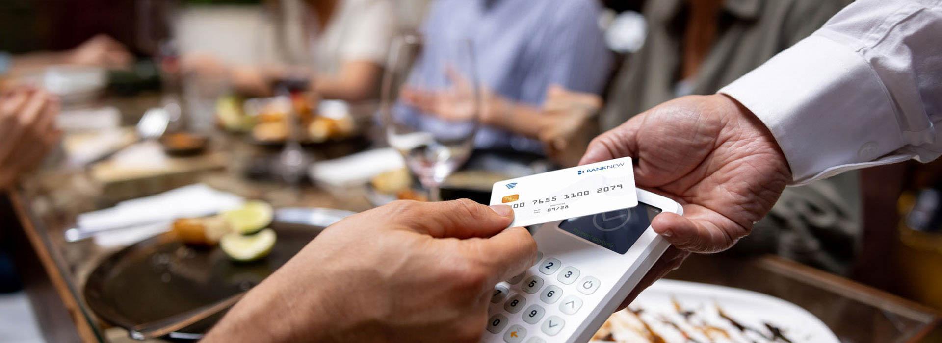 people having dinner and hand tapping credit card to pay bill