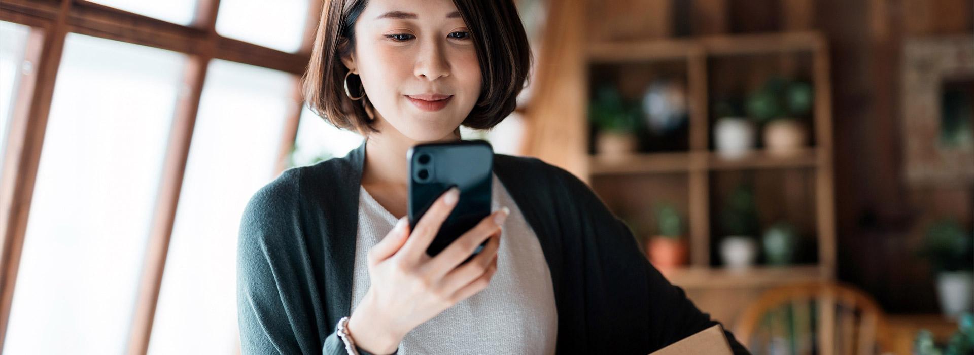 Woman of Asian descent holding a cellphone in her hand.
